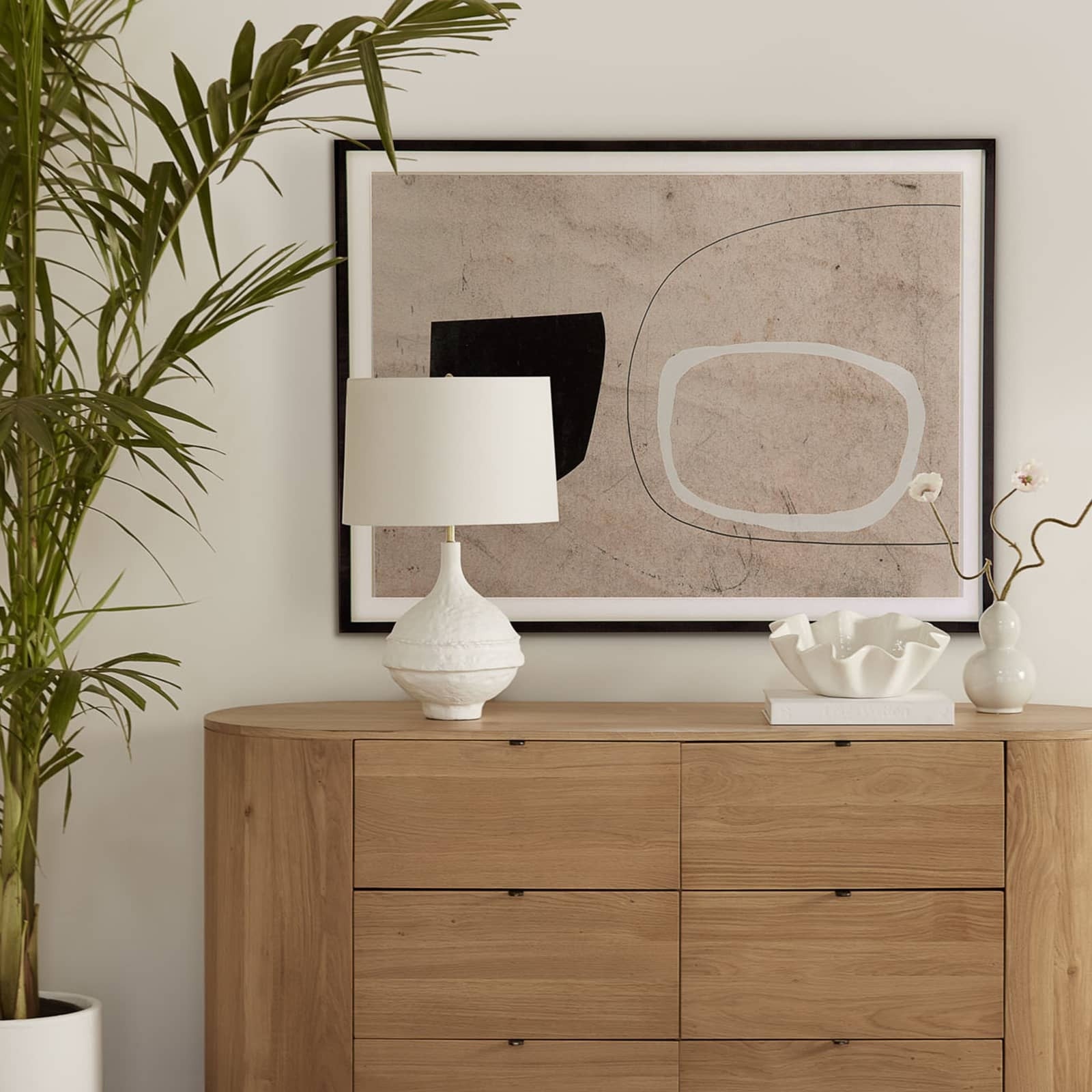 Wooden dresser with a lamp, abstract art, and decorative items in a room setting.