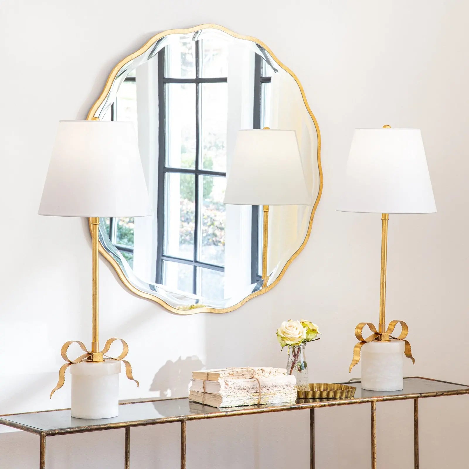 Decorative mirror with gold frame above a console table with lamps and decorative items.