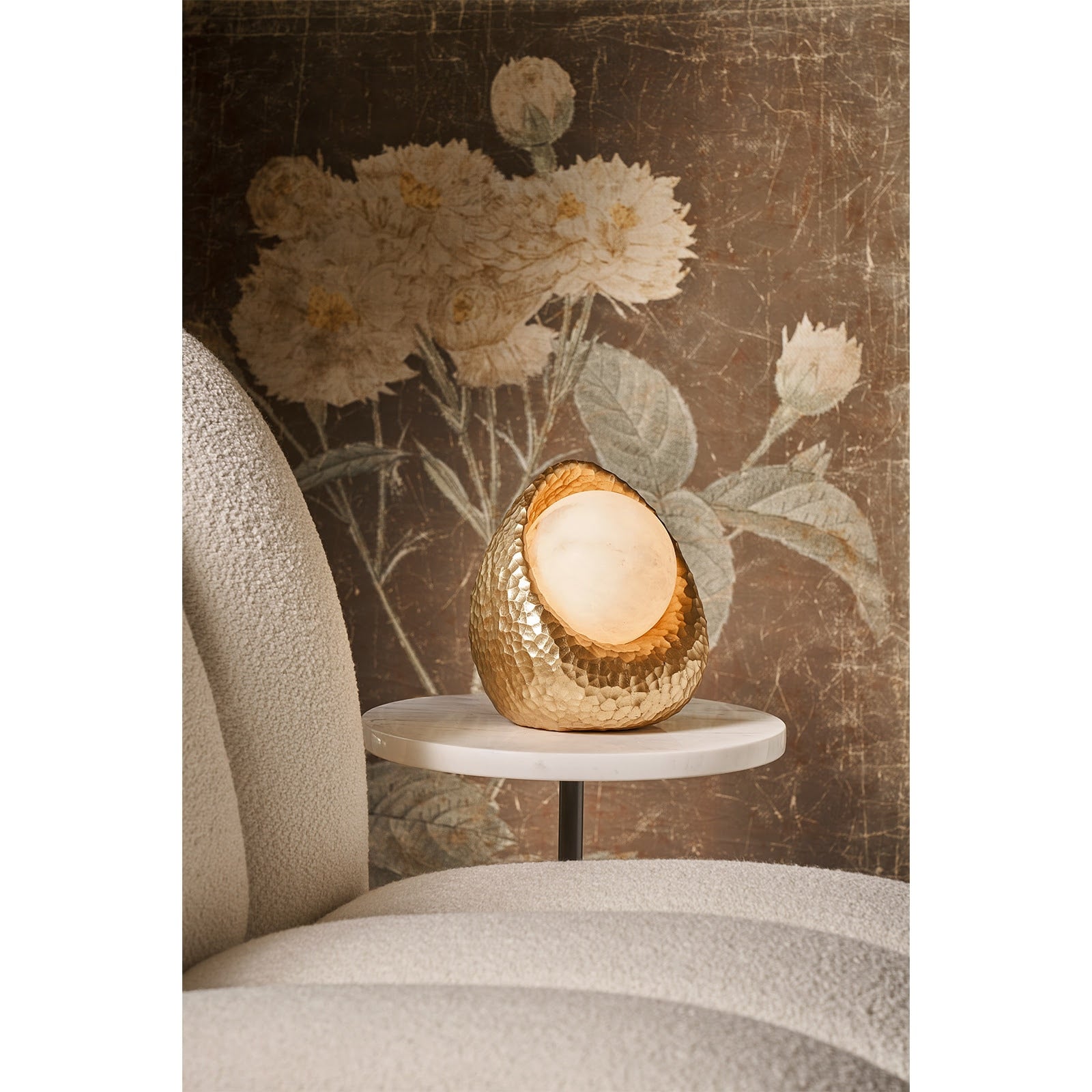 Nest Mini Lamp, a small decorative light fixture with an intricate gold resin hammered base and a round, soft glowing alabaster sphere.