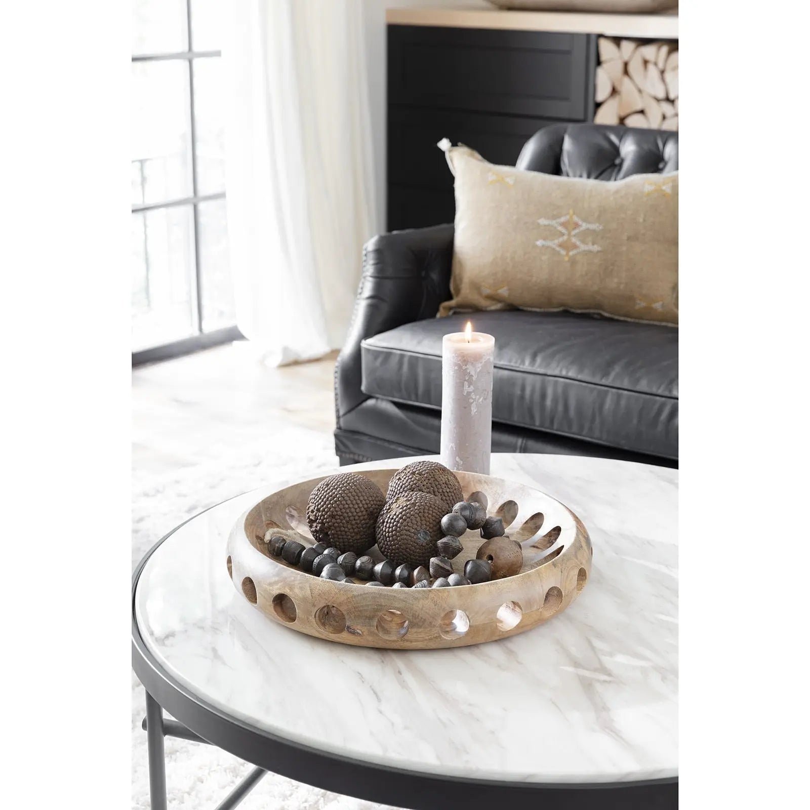 Decorative bowl with stones and a candle on a marble table in a living room.