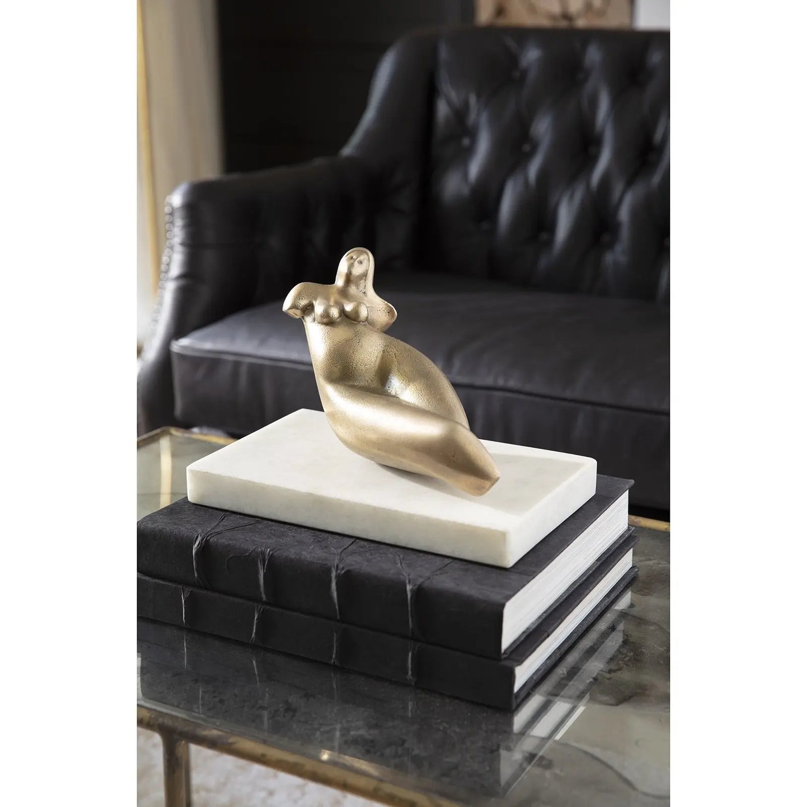 Gold sculpture on a white base on a black leather ottoman