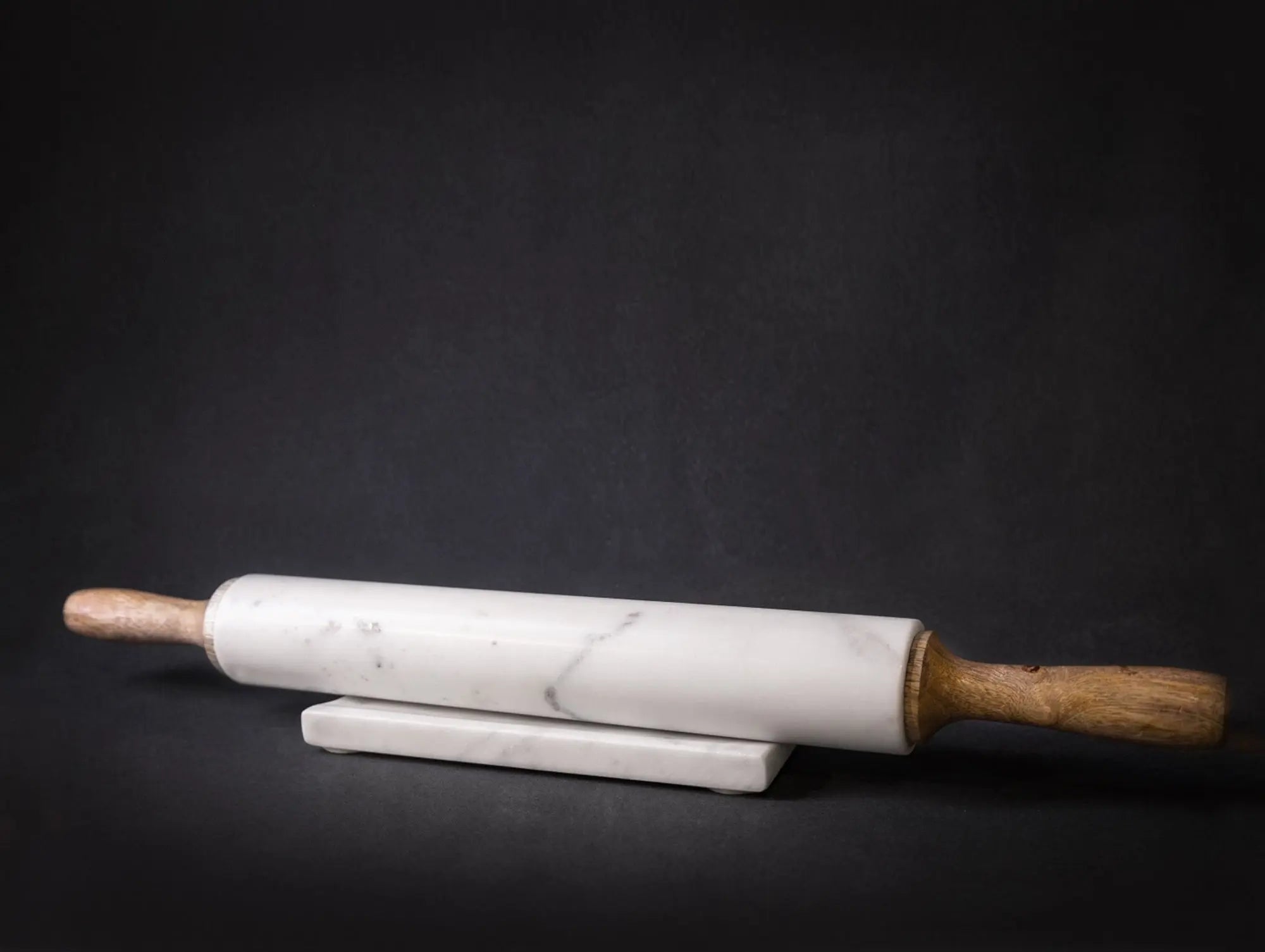 A professional 18-inch rolling pin featuring a white marble center and tapered mango wood handles, resting on a matching marble and wood storage cradle.