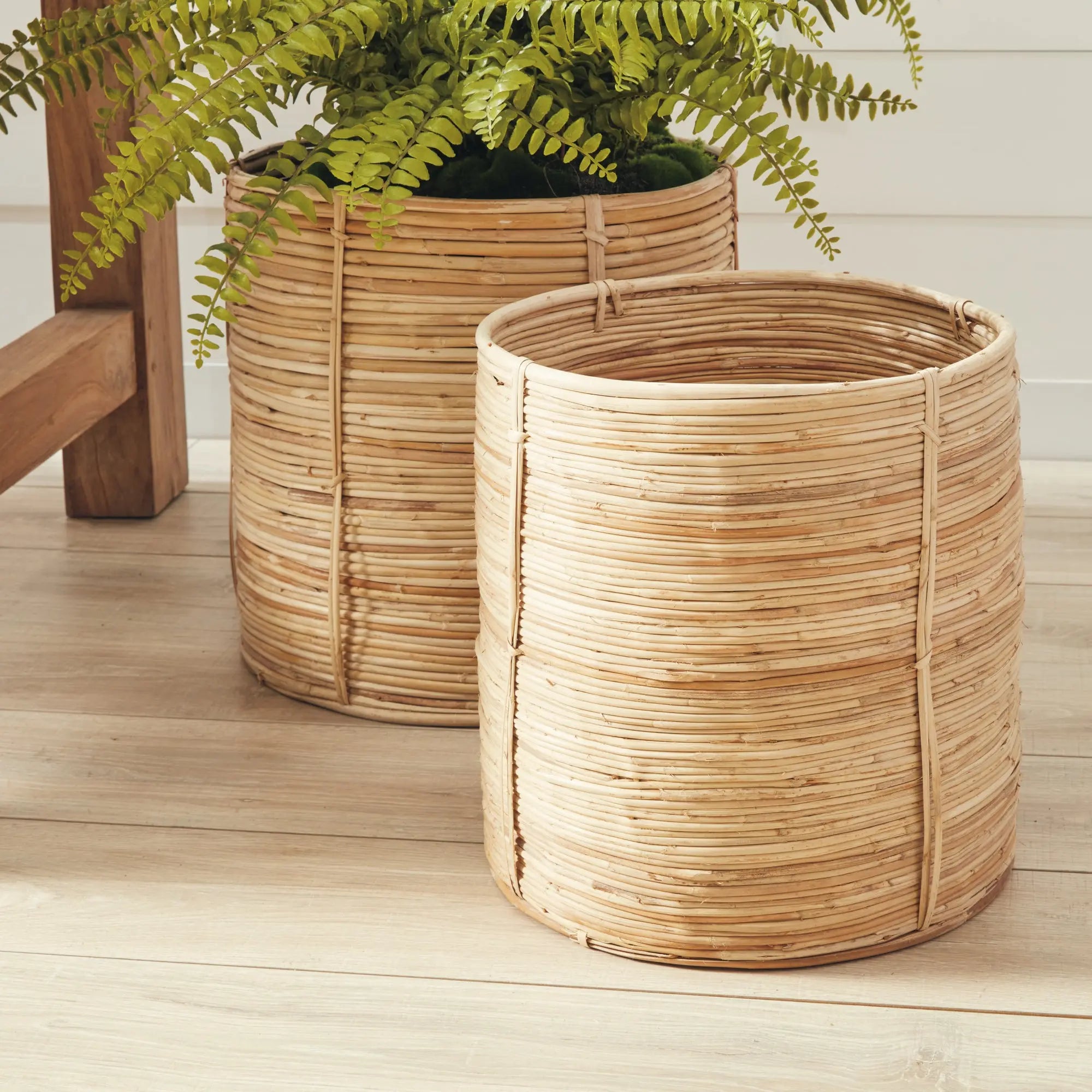 Two woven planters on a wooden surface with a plant inside one of them.