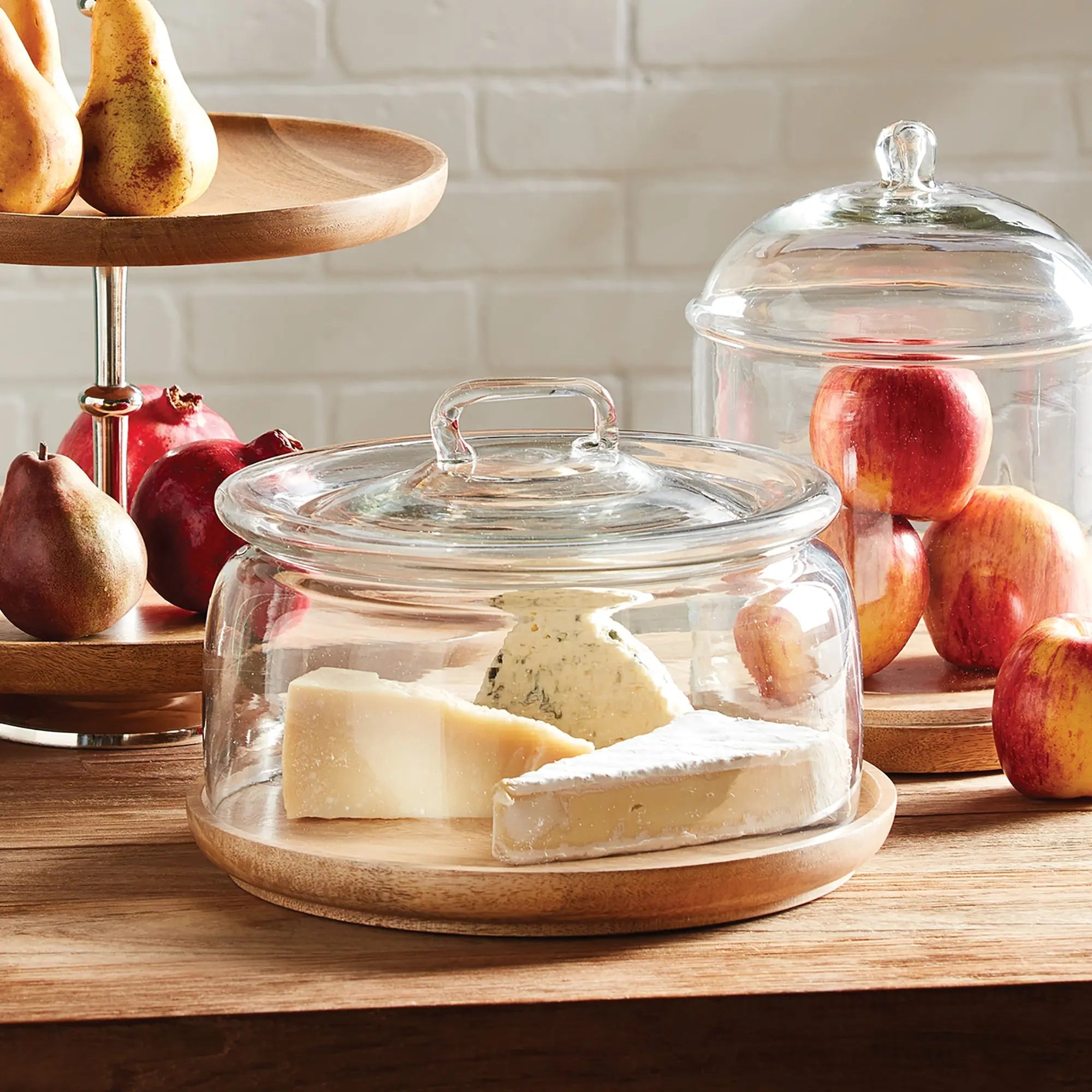 Adrien cloche with a clear glass dome on a round, natural wood tray, styled for serving pastries or cheese.