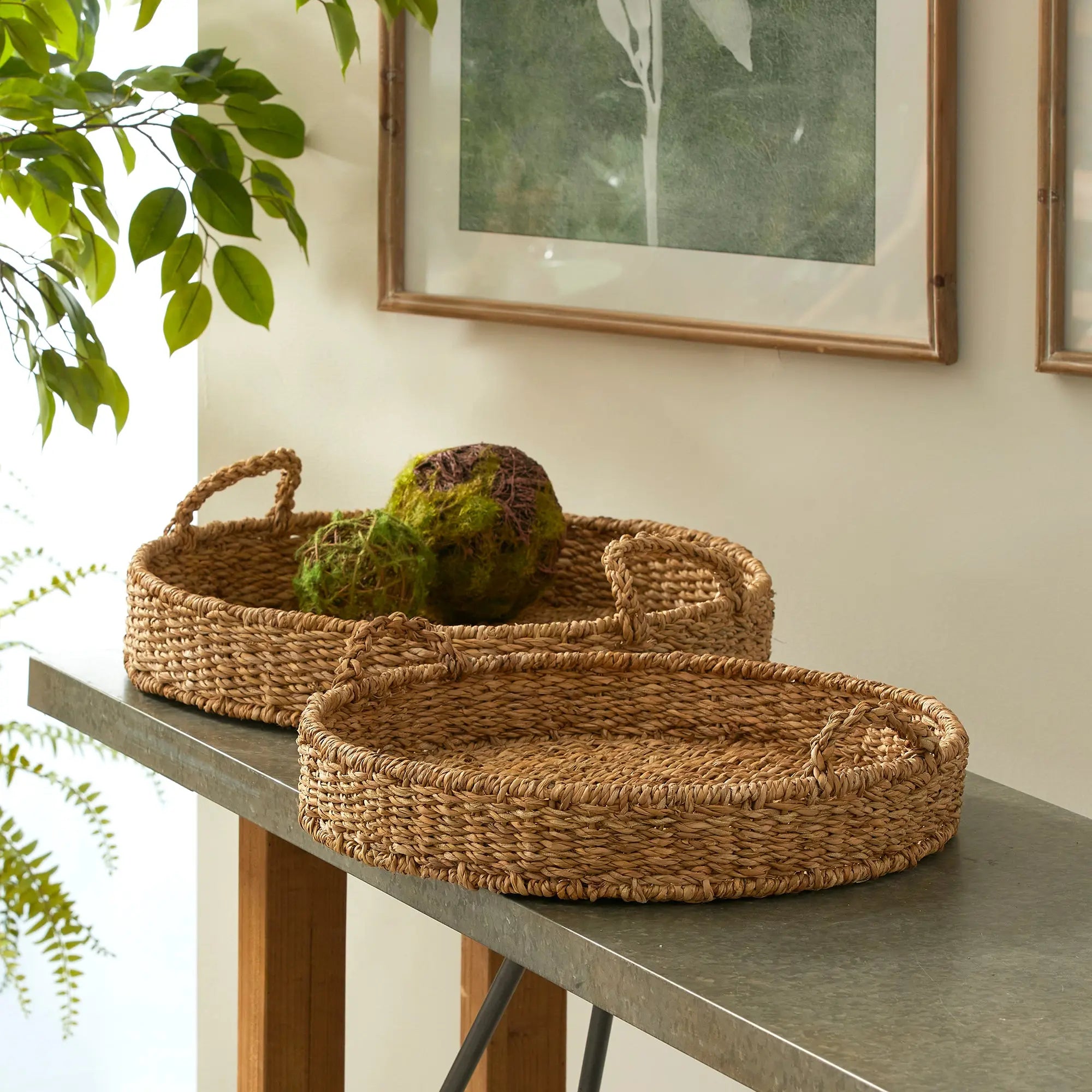Two woven baskets on a table with a plant and framed picture in the background