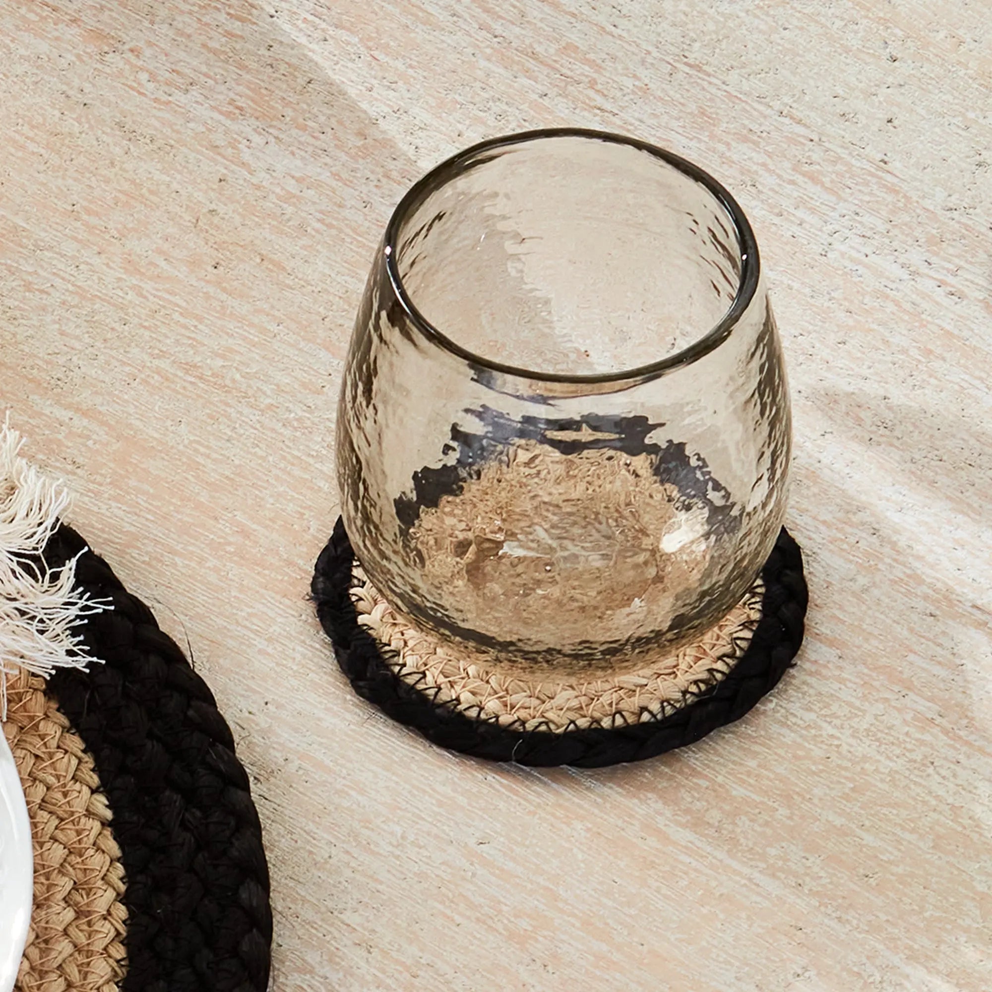 Clear glass candle holder on a woven coaster with a textured surface
