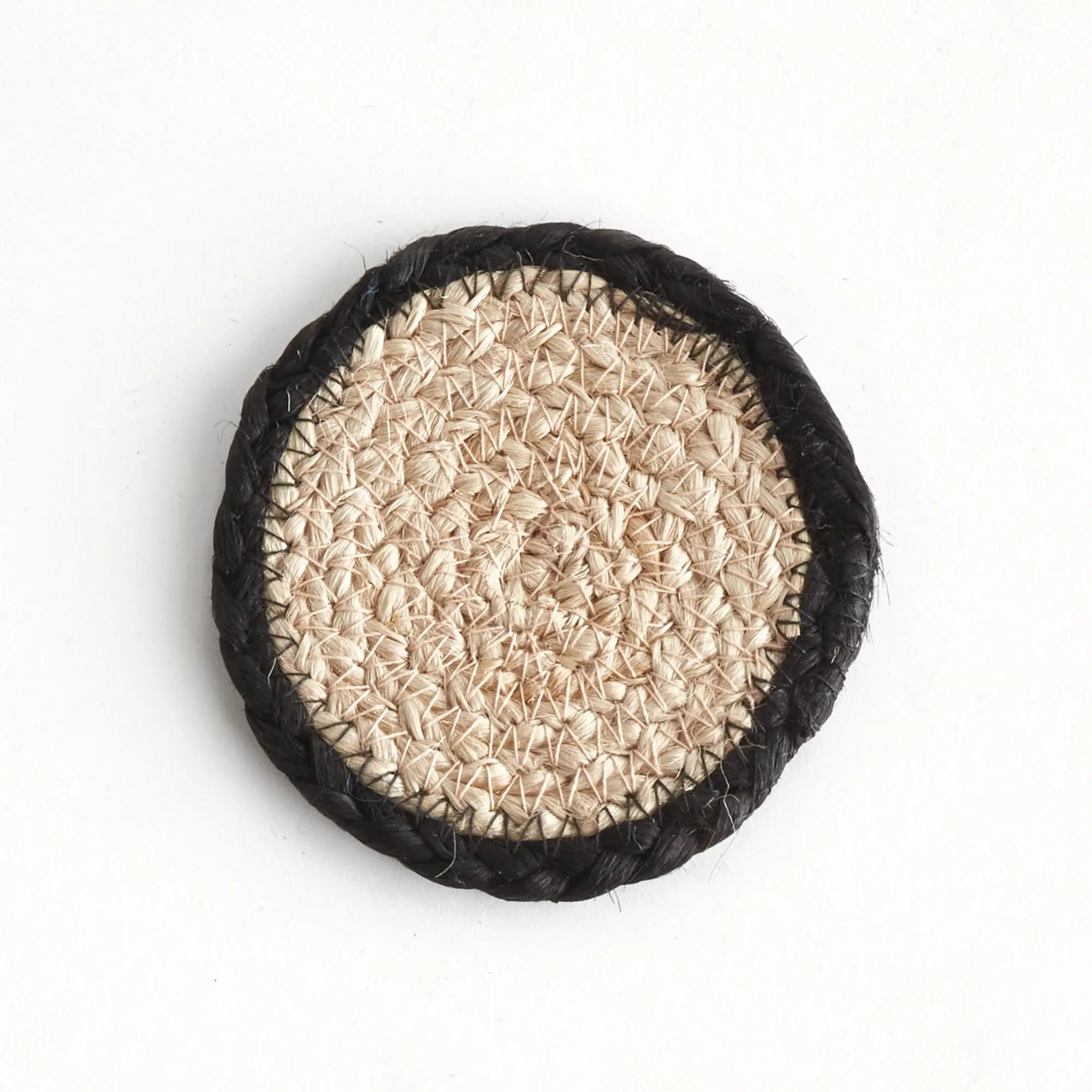Round natural fiber coaster with black rim on a white background