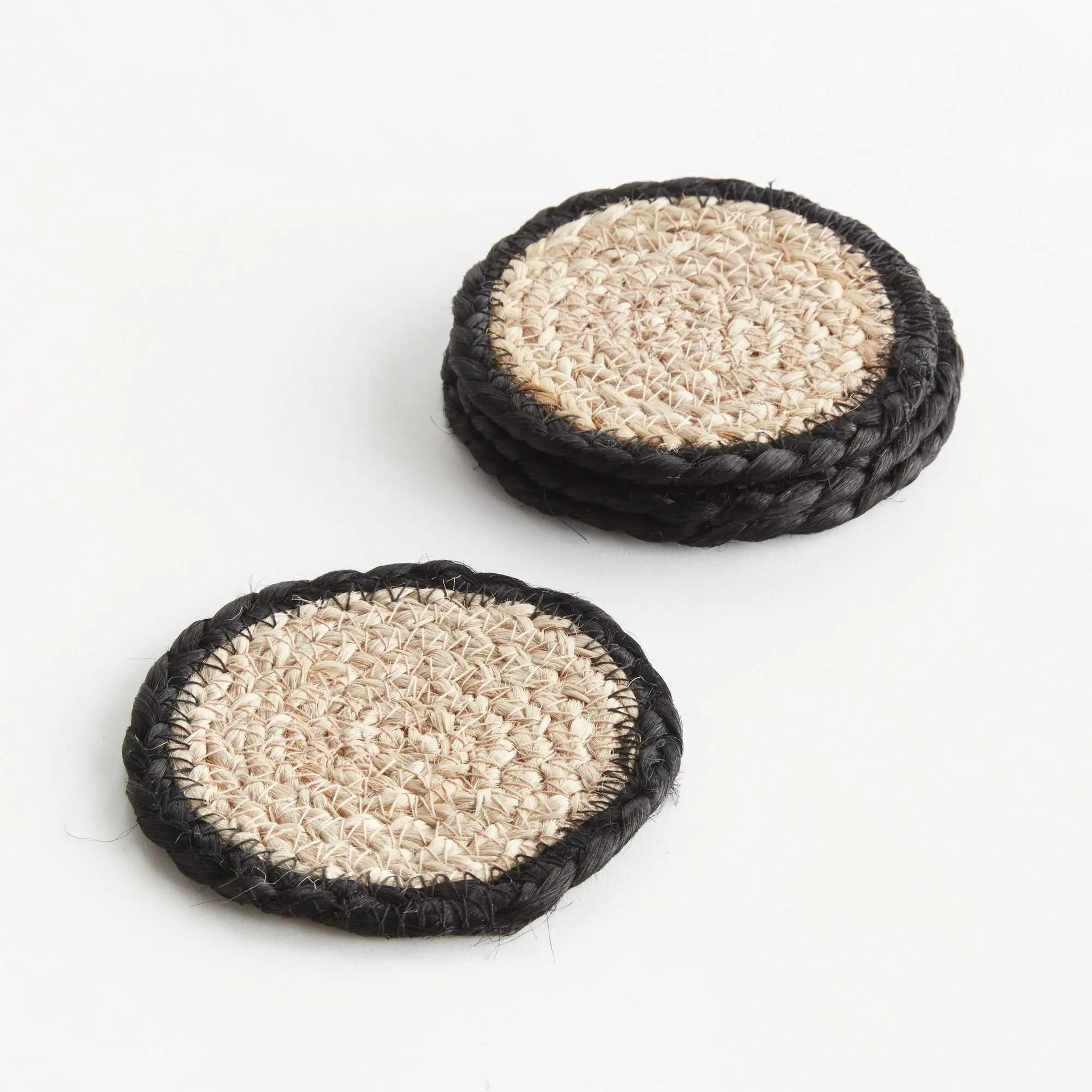 Two round woven coasters with black rims on a white background