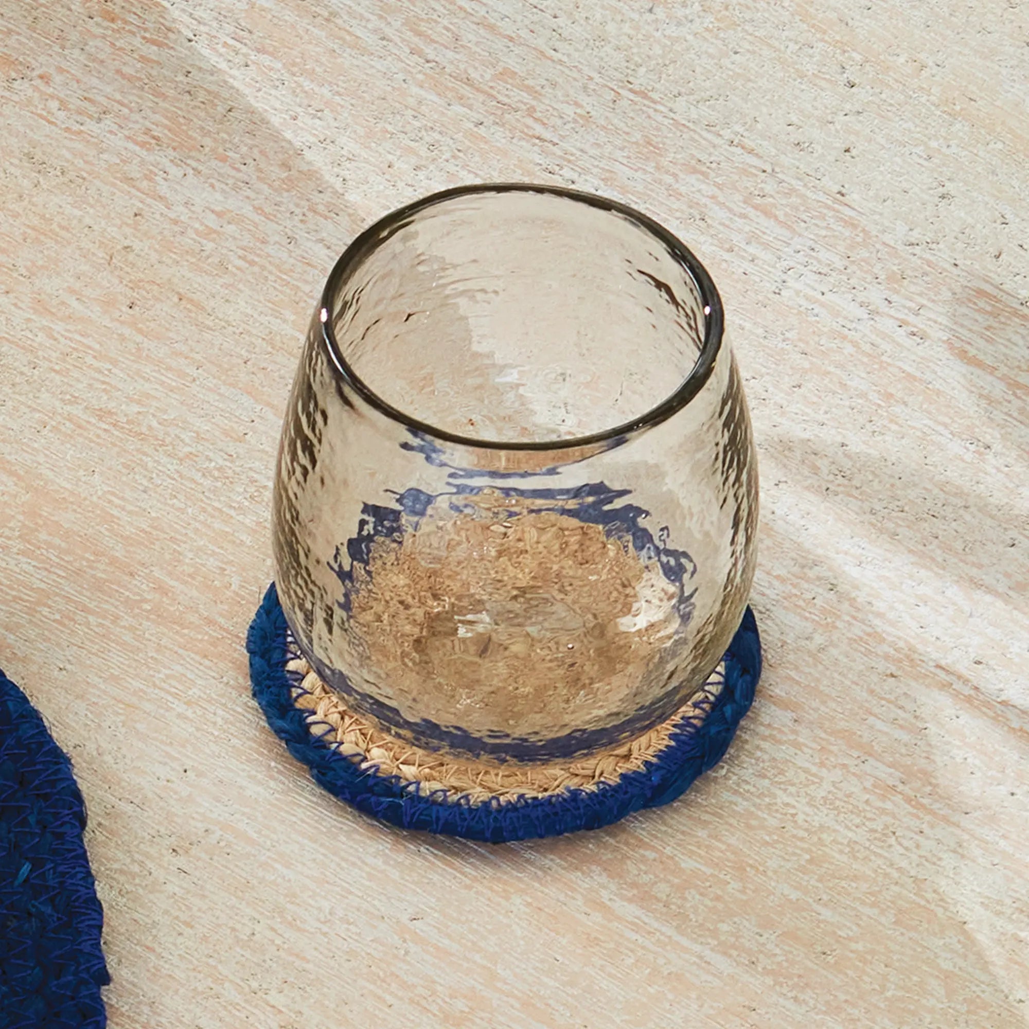 Clear glass on a blue woven coaster with a wooden surface background