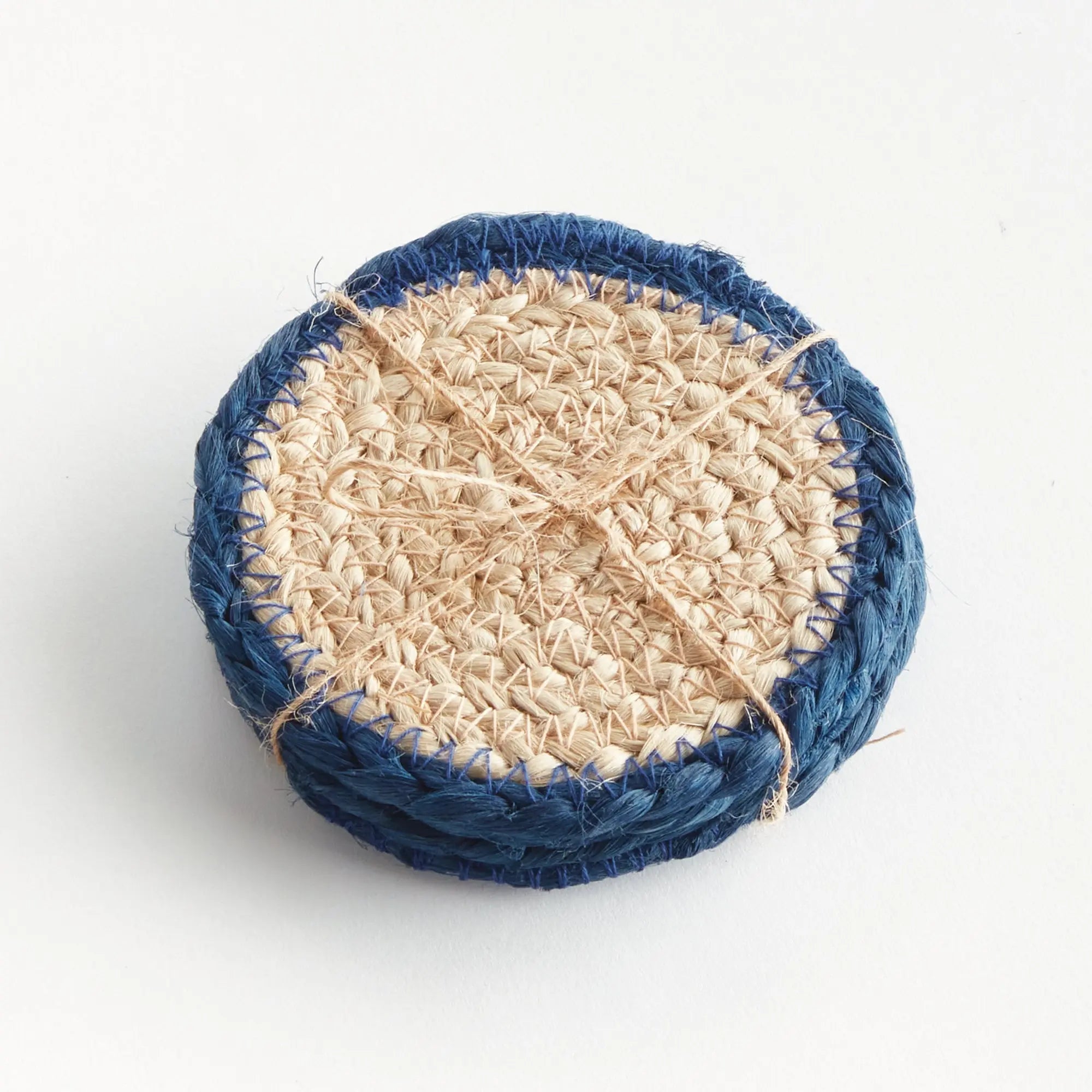 Coaster with natural fiber center and blue woven rim on a white background