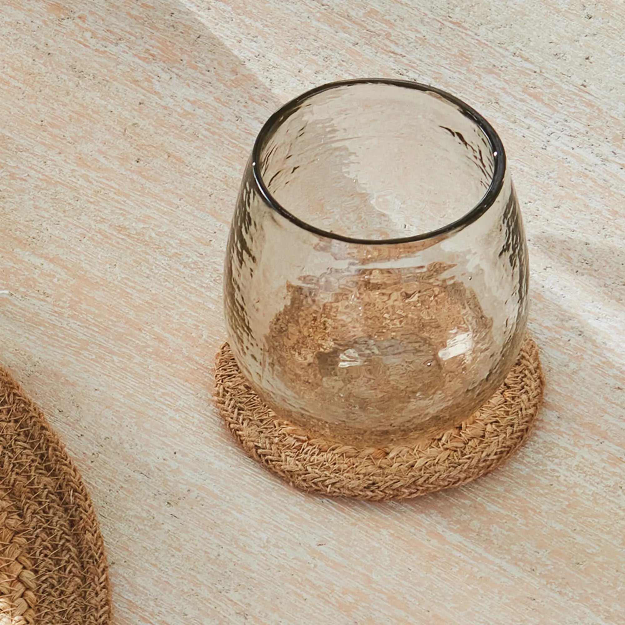 Clear glass candle holder on a woven coaster with a wooden surface background