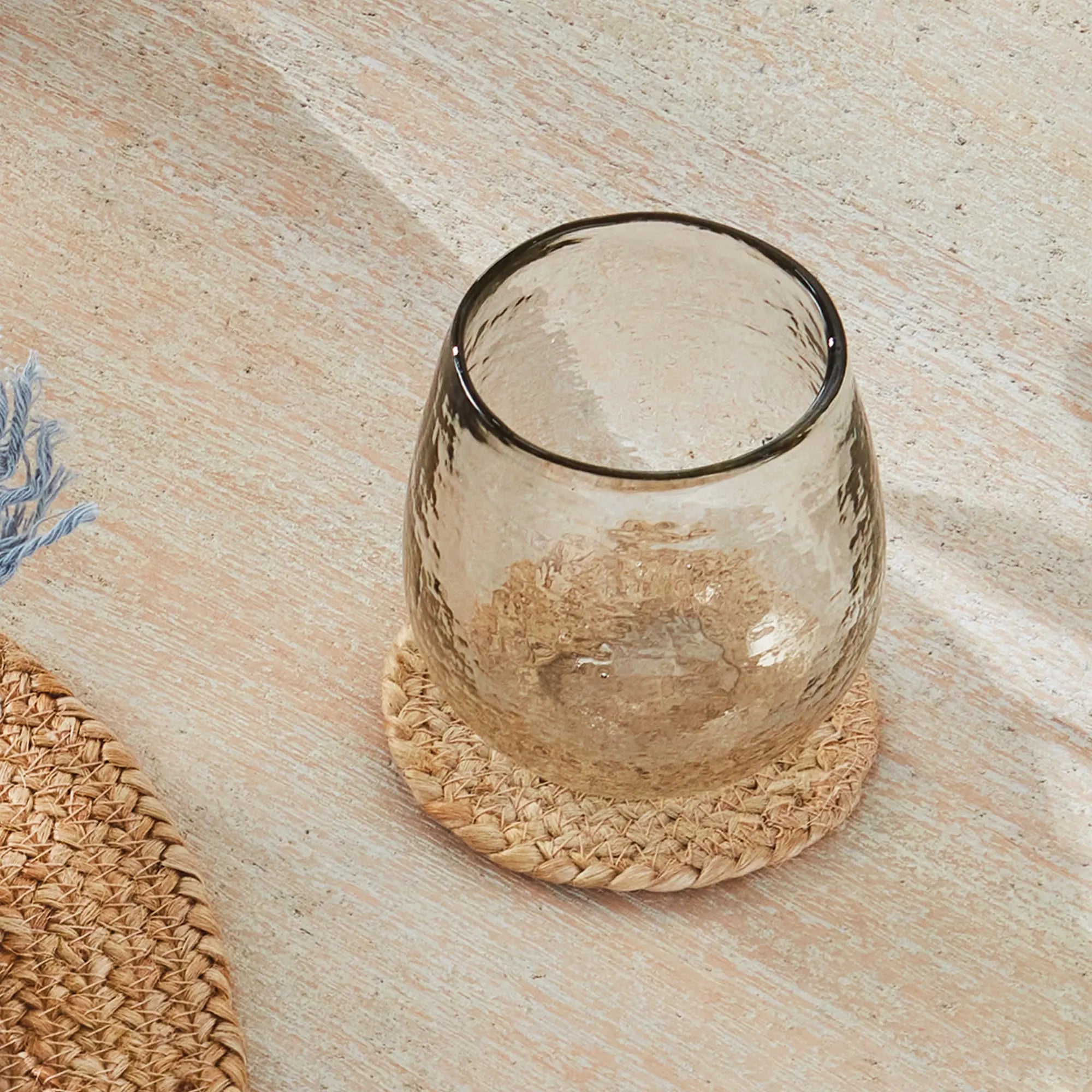 Clear glass candle holder on a woven coaster with a wooden surface background