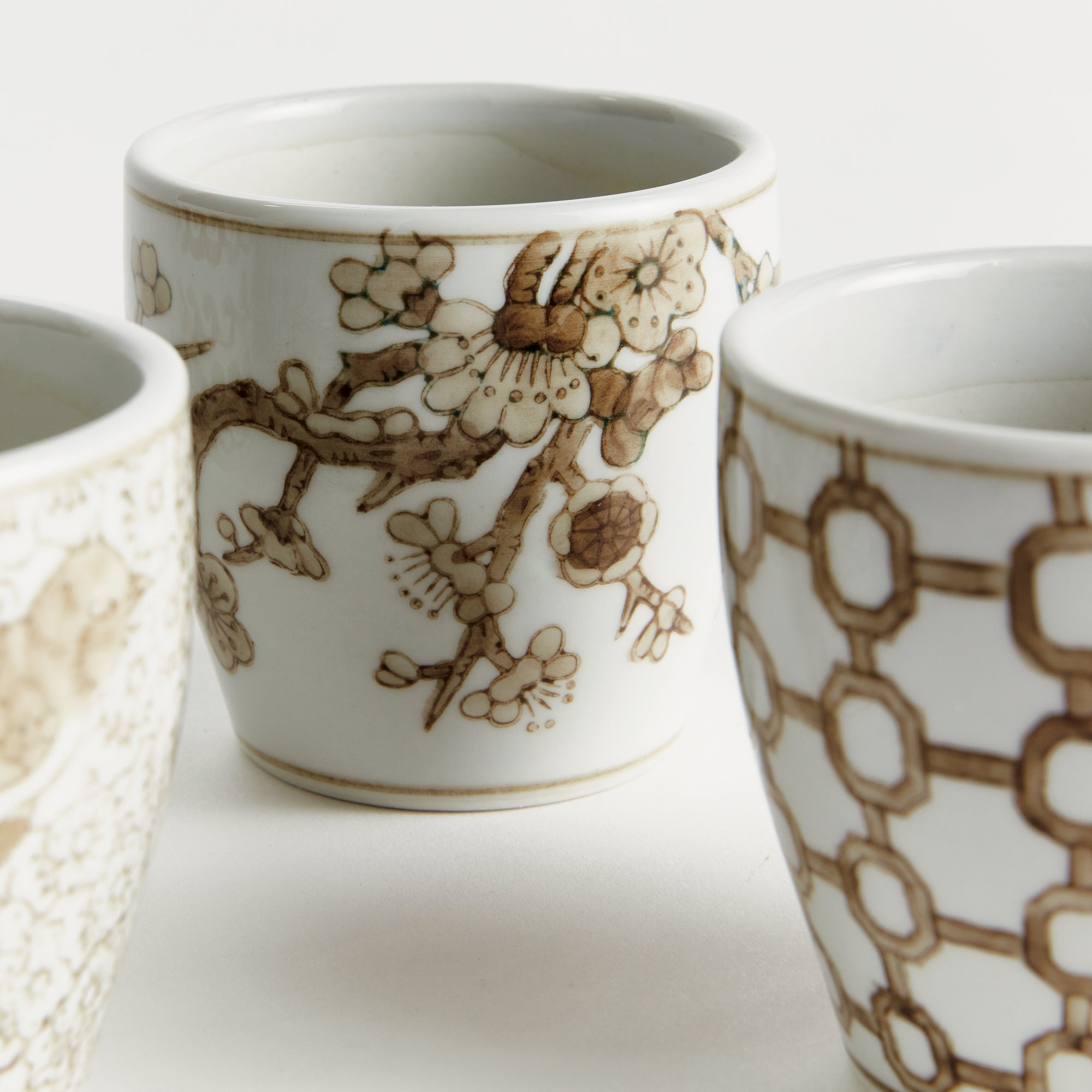 Three ceramic cups with intricate brown floral and geometric patterns on a white background