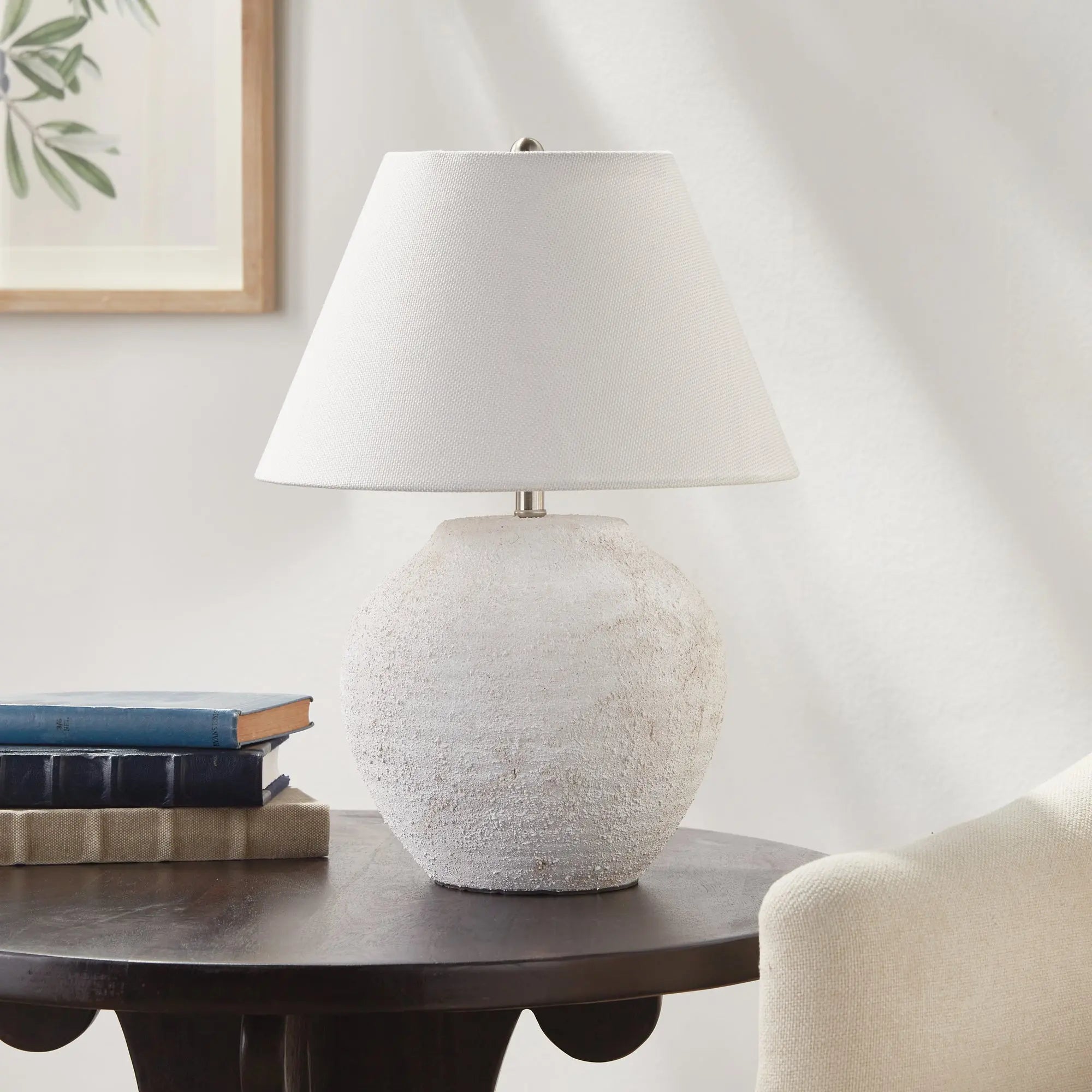 White textured theo table lamp on a wooden side table with books in a room setting.