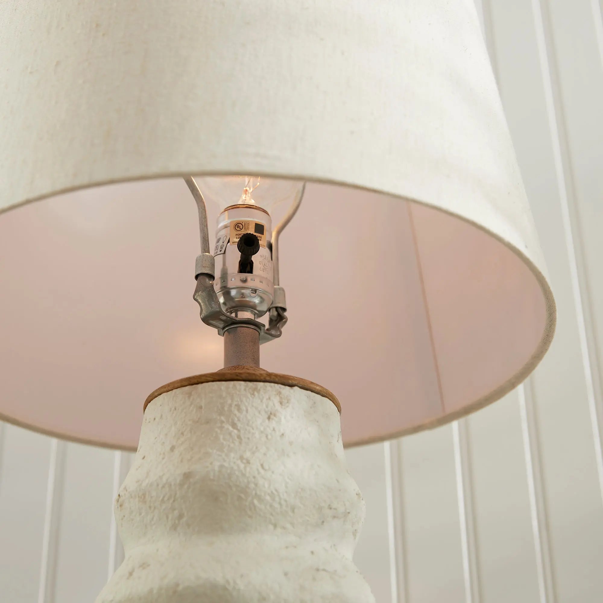 Adria Table Lamp with a textured, pitted, warm white ecomix base and a cream-colored tapered lamp shade. The lamp is shown from the front against a neutral background.