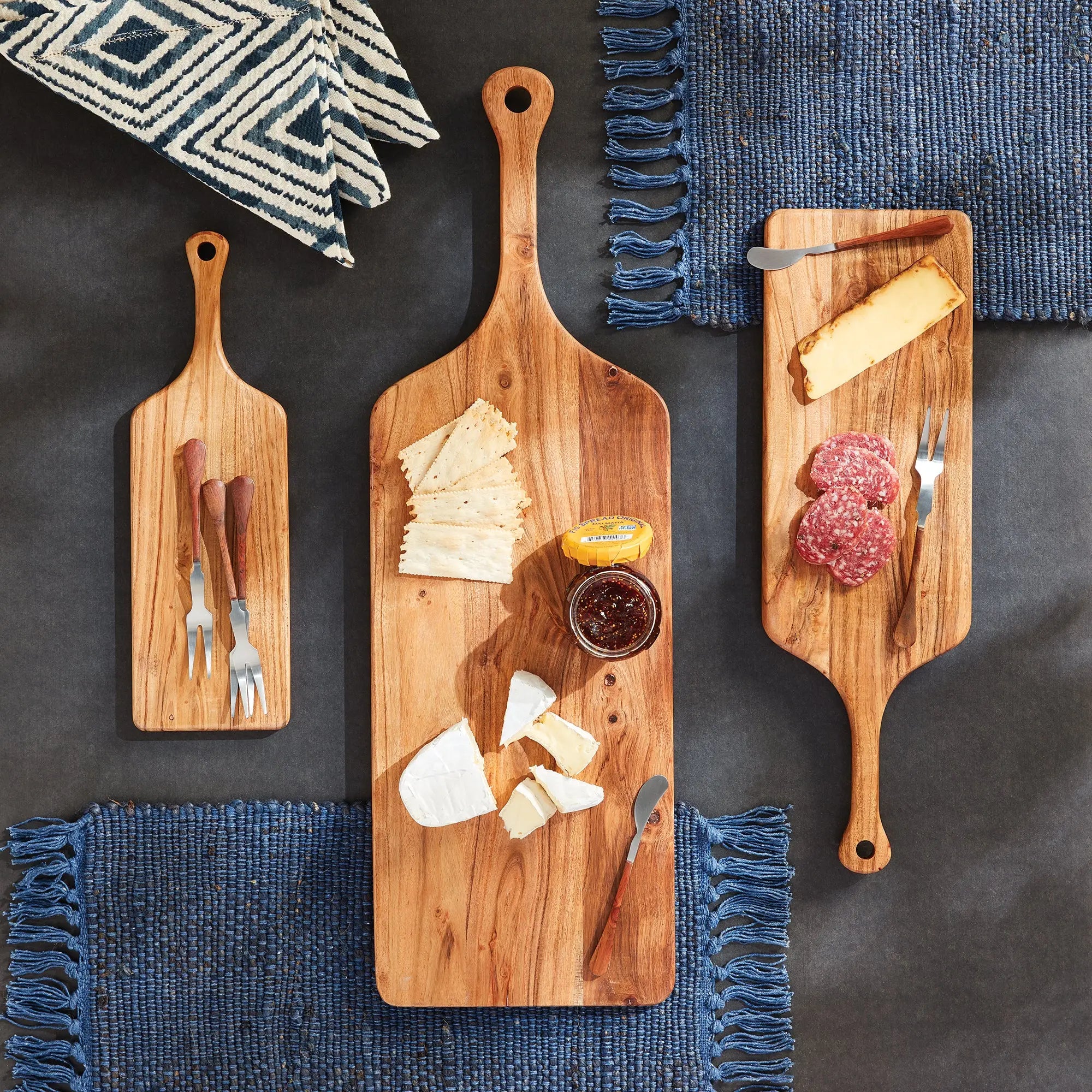 Three wooden cutting boards with various food items on a dark surface with blue placemats.
