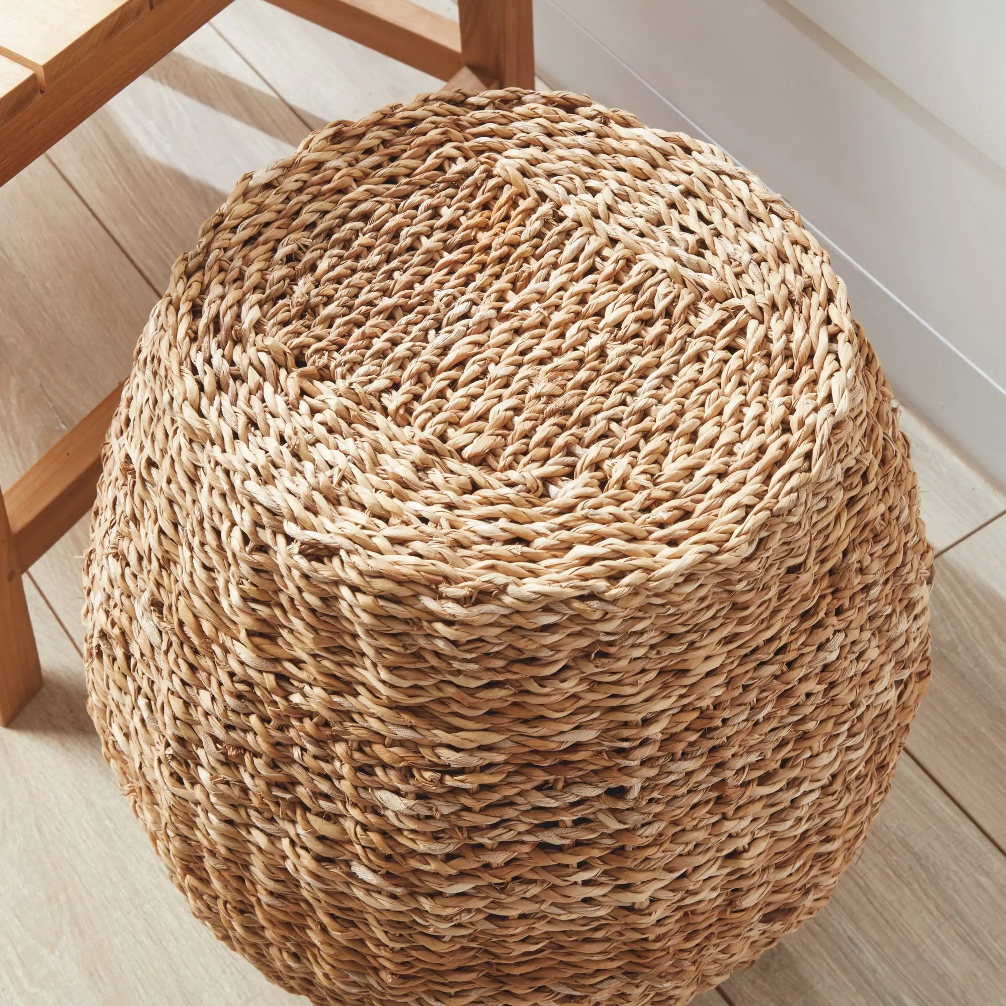 Natural seagrass hourglass pouf used as a side table with a book and coffee cup, showcasing its woven texture and versatile design.