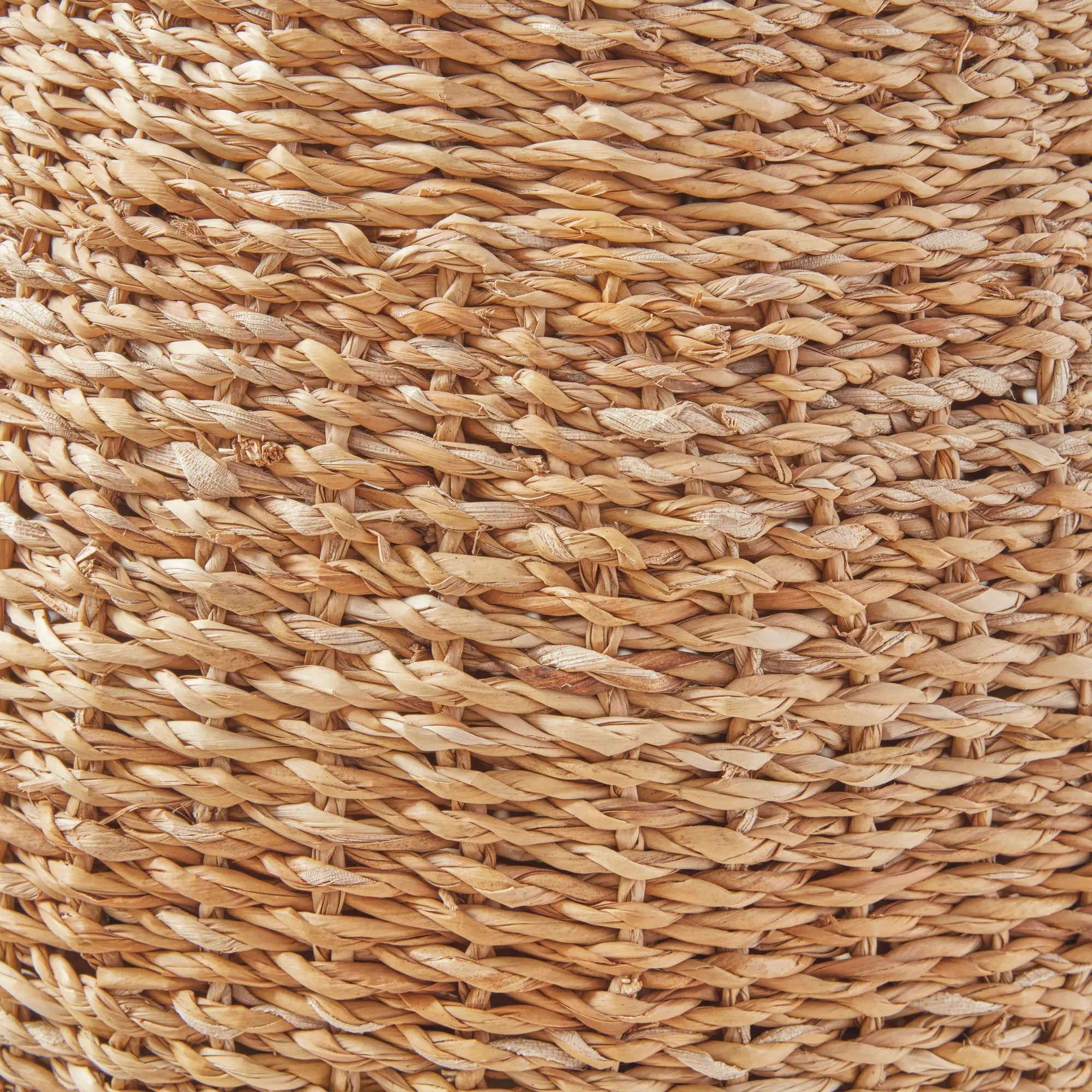 Natural seagrass hourglass pouf used as a side table with a book and coffee cup, showcasing its woven texture and versatile design.