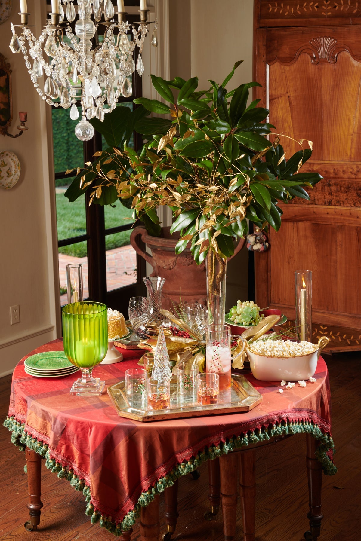 Decorative table setting with a chandelier, plant, and various items on a red tablecloth.