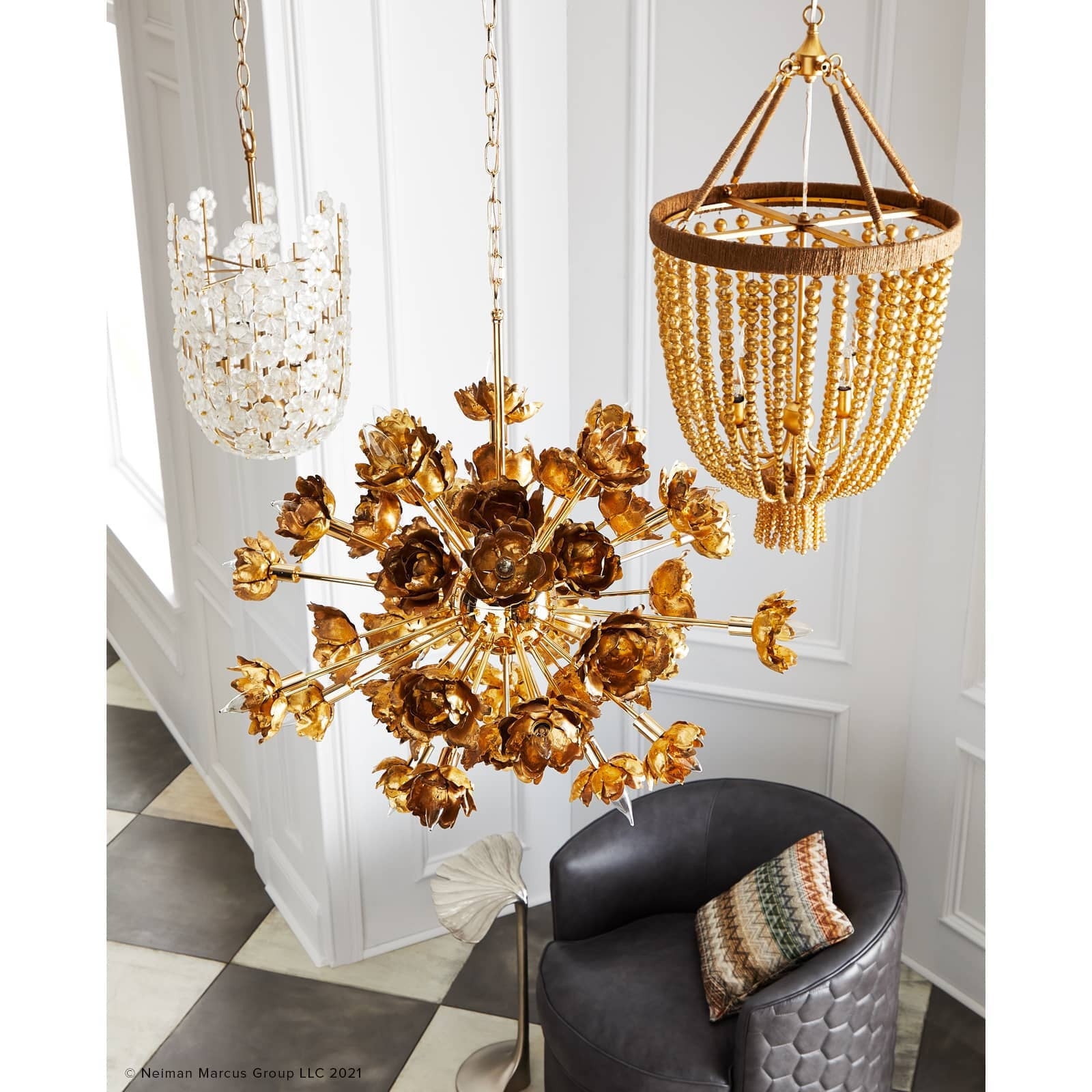 Gold floral chandelier hanging in a room with a black chair and decorative pillows.