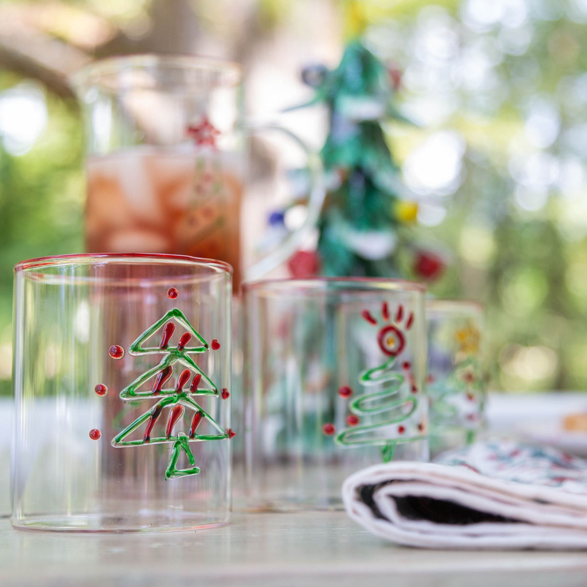 Two glass tumblers with Christmas tree designs on a table outdoors.