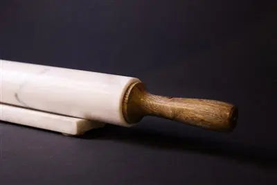 A professional 18-inch rolling pin featuring a white marble center and tapered mango wood handles, resting on a matching marble and wood storage cradle.