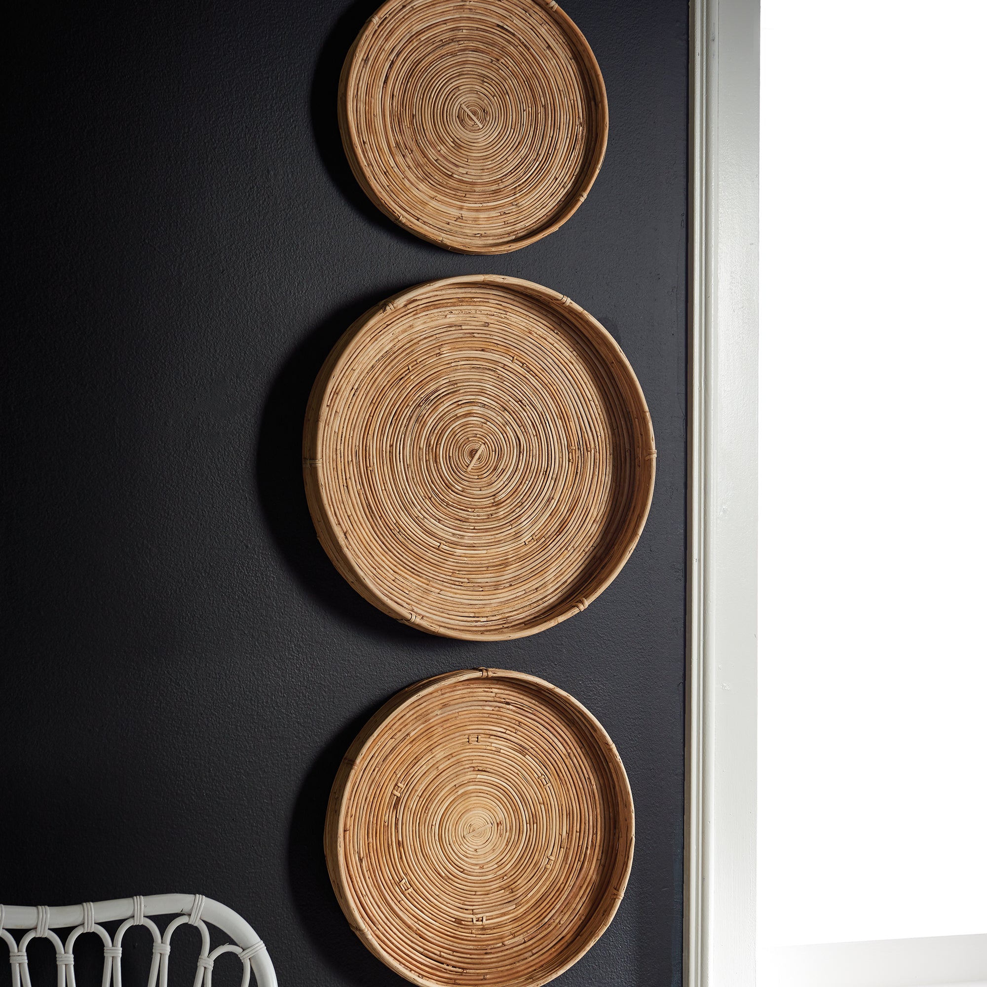 Three woven baskets of different sizes on a dark surface with a white chair partially visible.