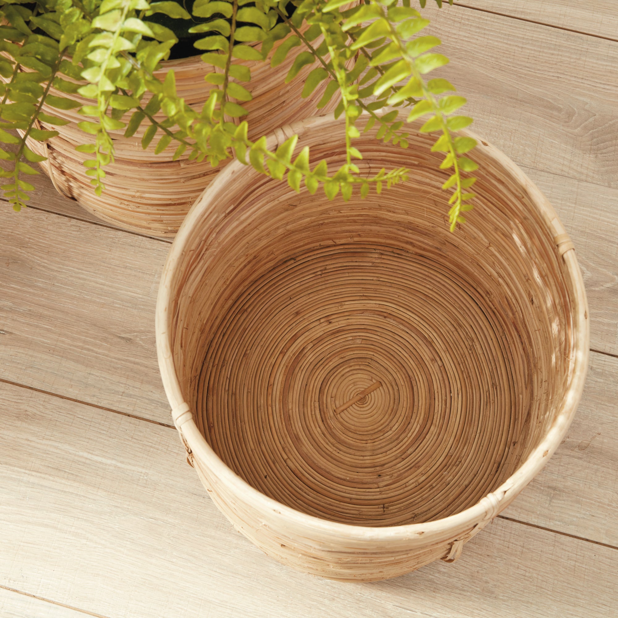 Woven plant pot on a wooden surface with a plant partially visible.