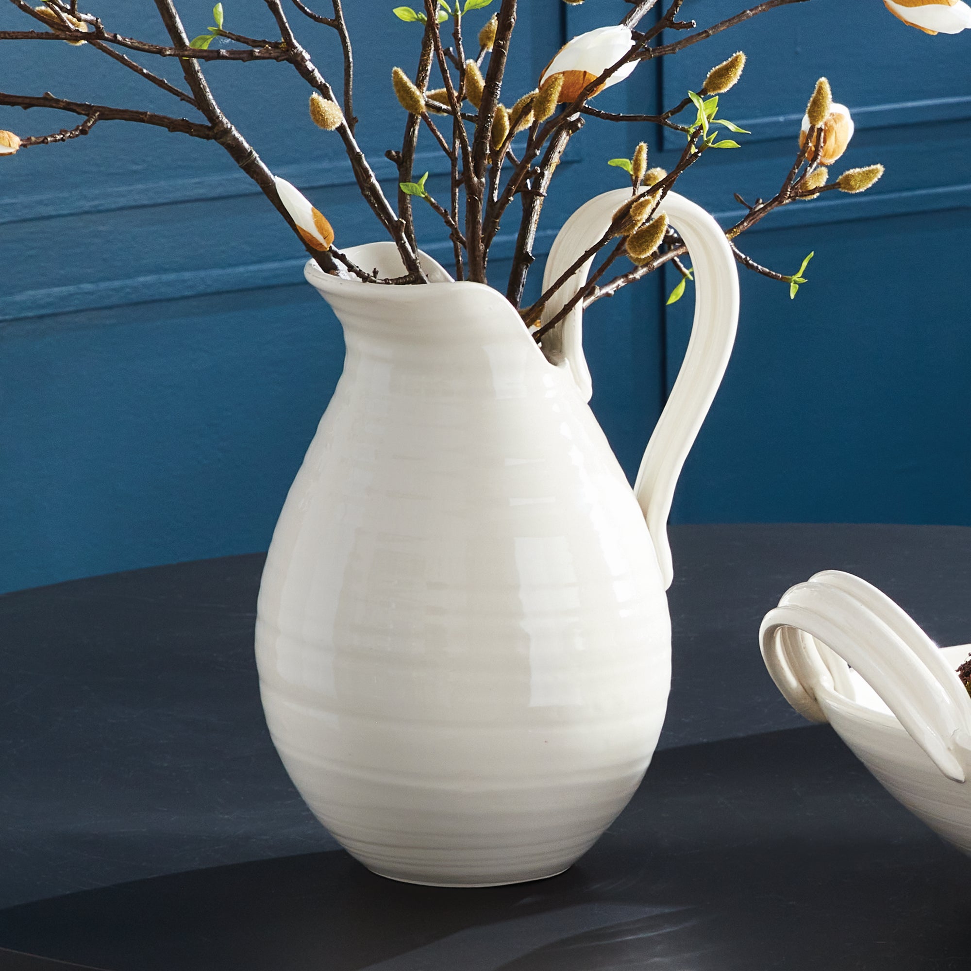 White ceramic pitcher with floral arrangement against a blue background