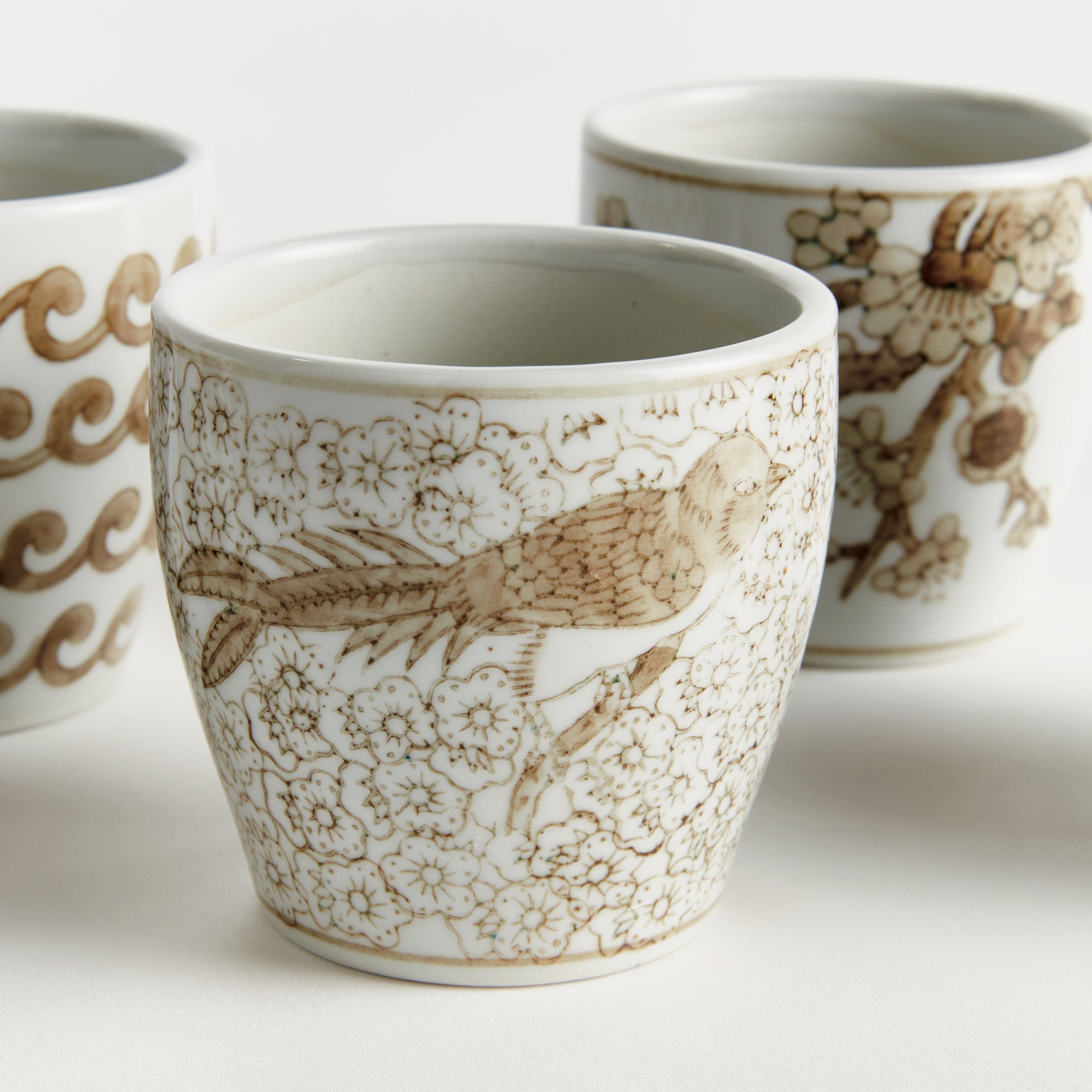 Three ceramic cups with intricate brown patterns on a white background